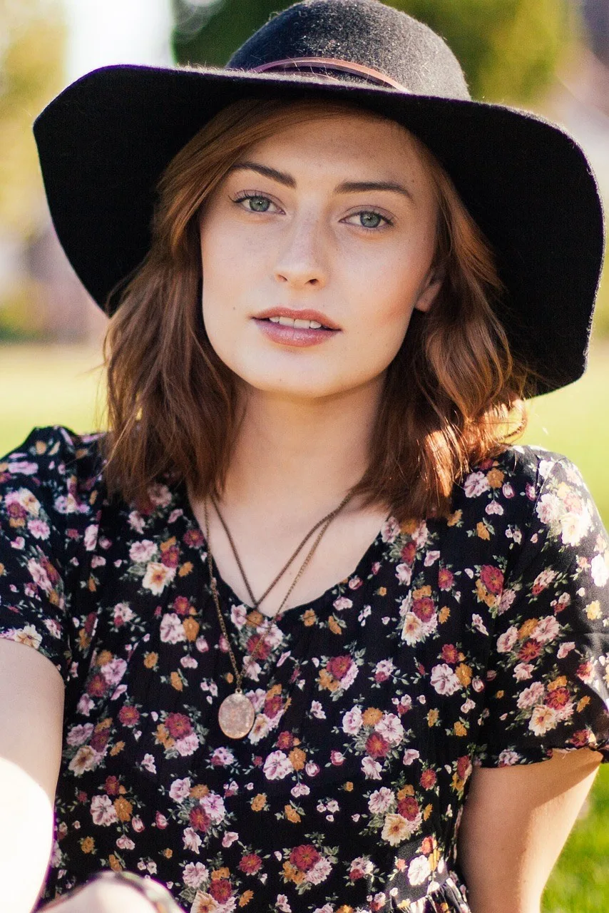 Une femme en robe à fleur le regard pensif, elle porte un chapeau